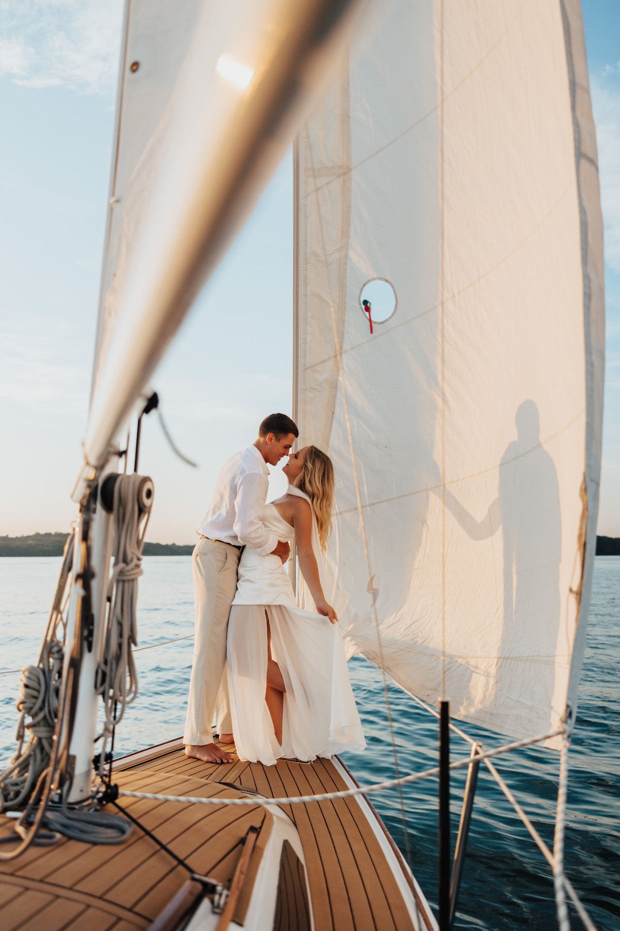 Couple in white standing on a sailboat bow in golden light