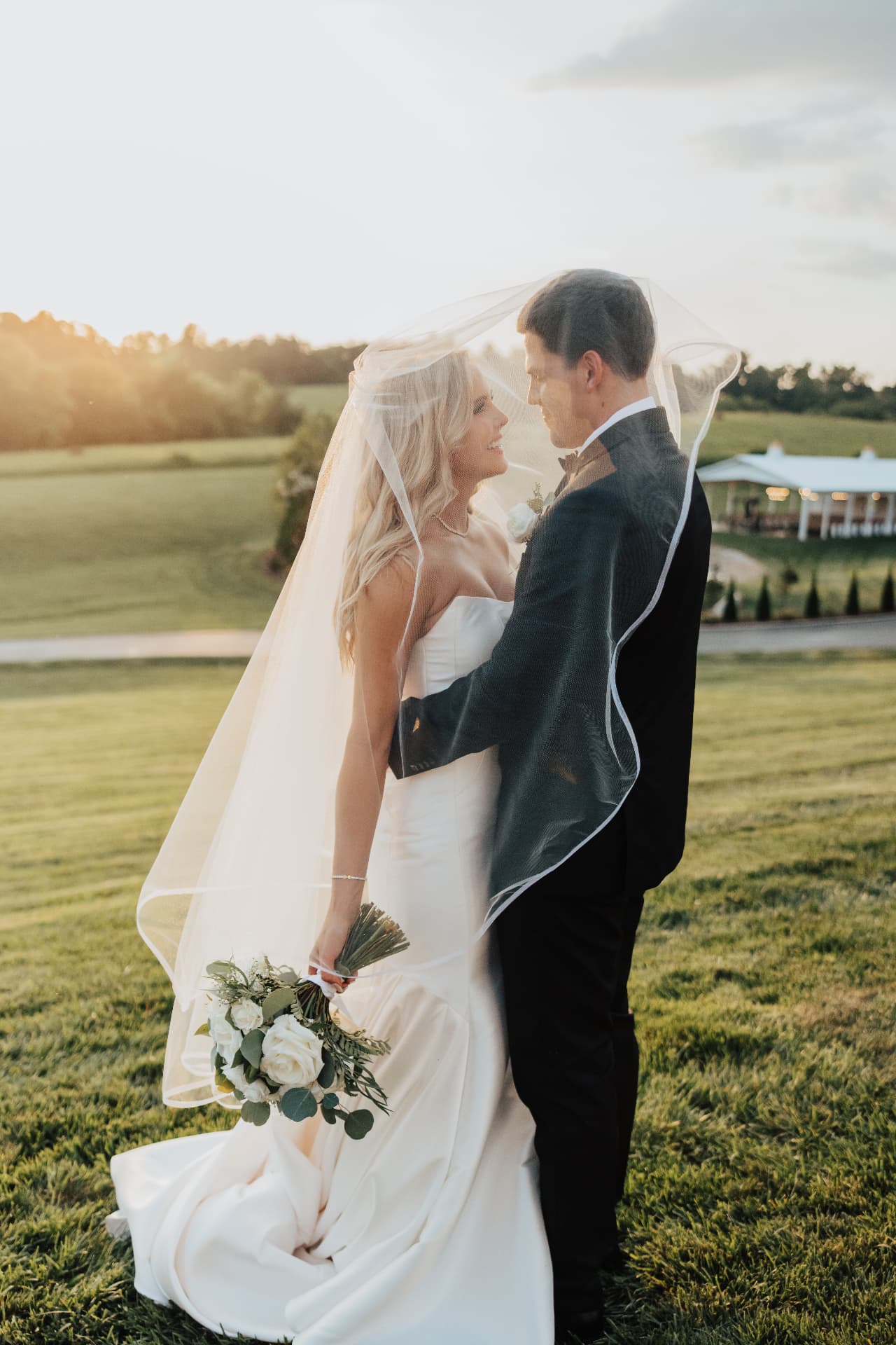 Couple standing face to face beneath a flowing veil at sunset