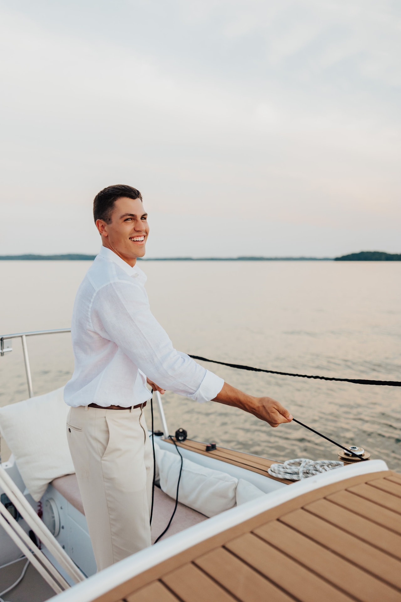 Man in white linen trimming a line at the helm of a sailboat