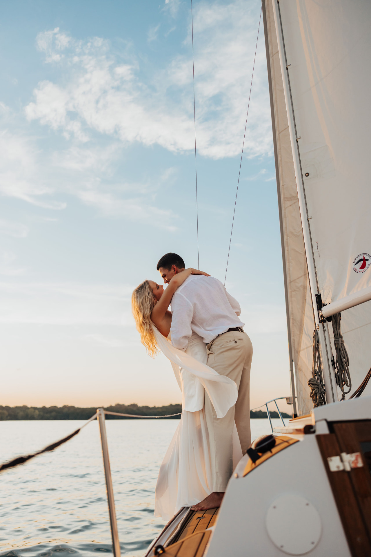 Man dipping woman in a flowing dress on a sailboat at dusk