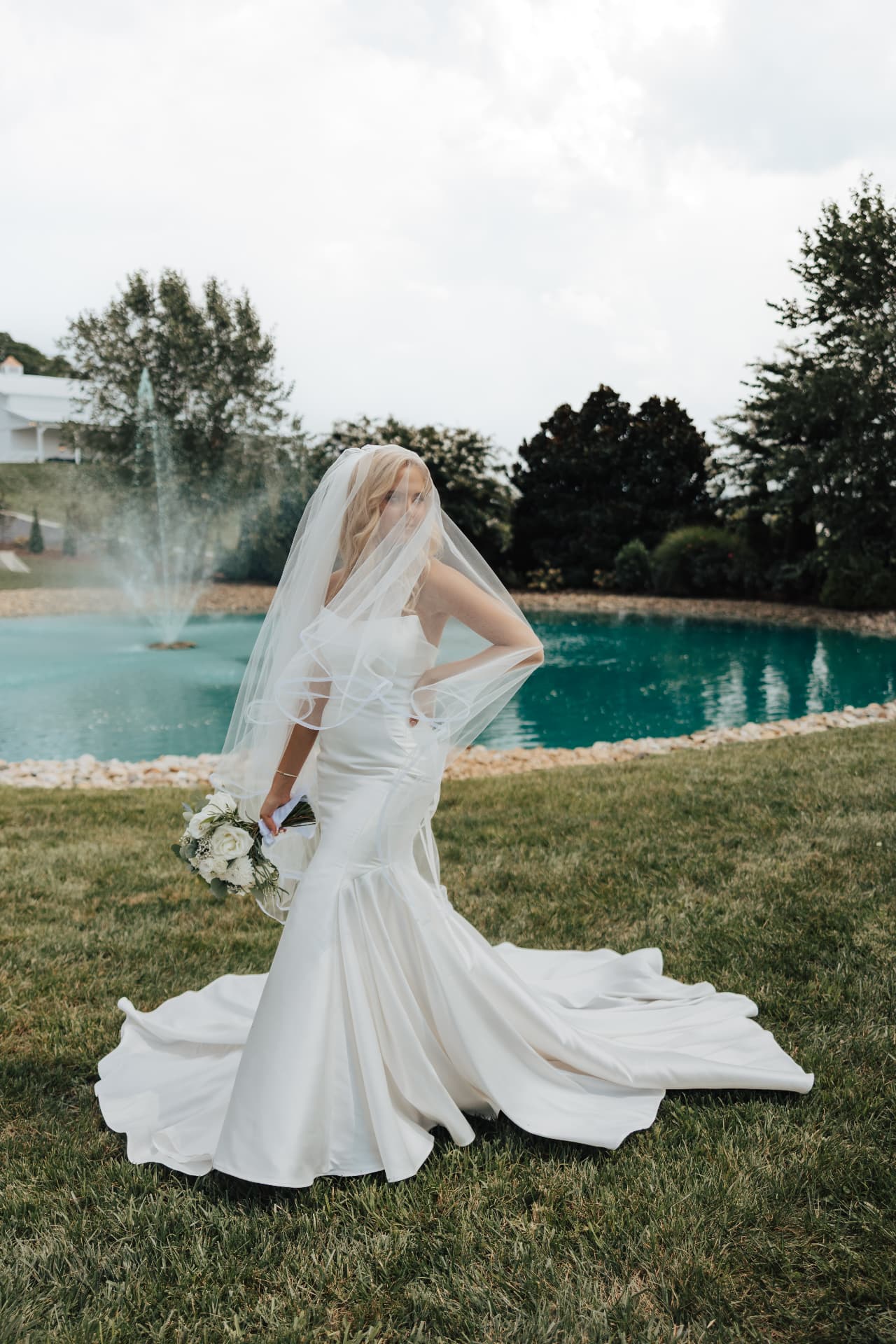 Bride with veil over her face standing before a fountain pond