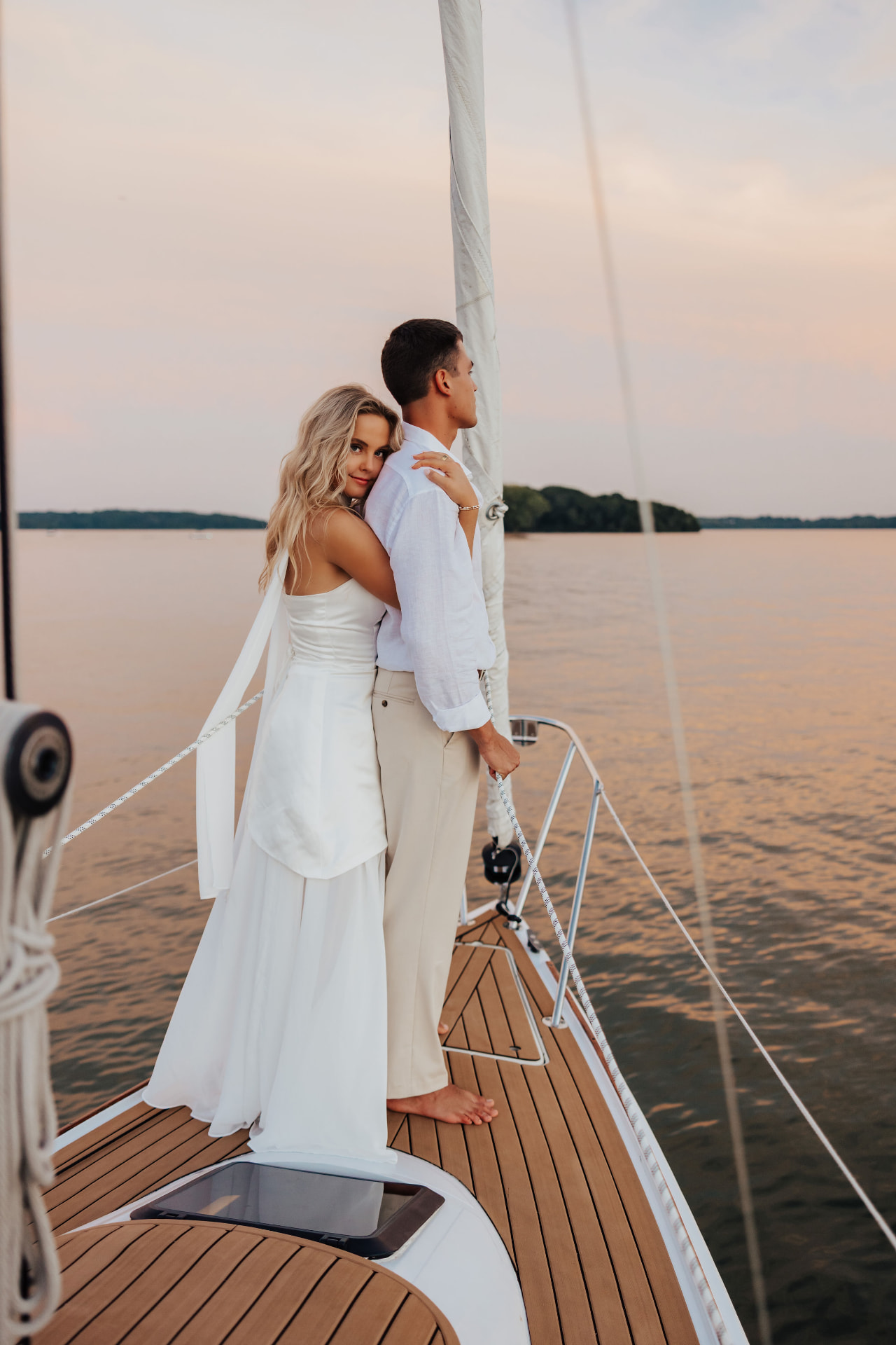 Couple standing at the bow of a sailboat under a pink sky