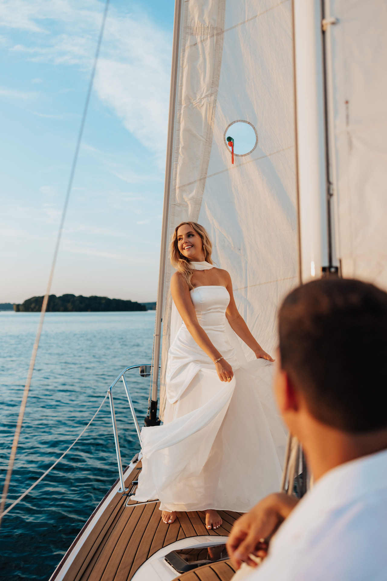 Woman in a white gown on a sailboat deck backlit by the sun