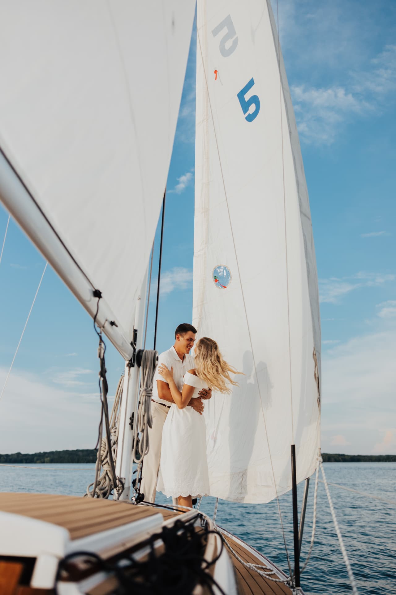 Couple embracing beside a full white sail on a lake